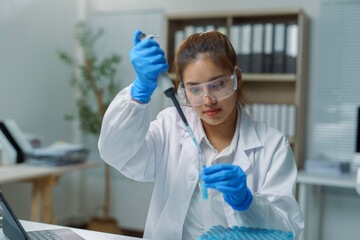 Scientist using micropipette dropping blue liquid into test tube in laboratory