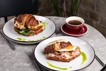 Two croissant sandwiches served on whiteplates with cup of rich coffee. The cozy cafe atmosphere enhances the delightful breakfast experience