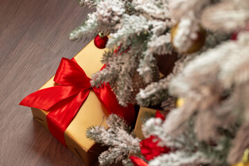 Top-down view of gifts in gold boxes with red bows under a snow-covered Christmas tree