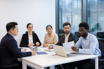Office workers, in business suits sitting at desk, talking and discussing details of new project...