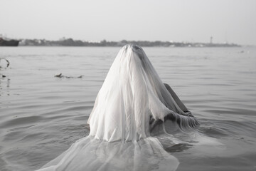An Indian man taking a holy dip in the river ganges during early morning covering his face with a...