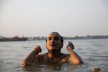 An Indian man taking a holy dip in the river ganges during early morning. he is chest deep...