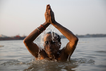 An Indian man taking a holy dip in the river ganges during early morning. he is chest deep...