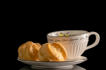 Ceramic cup with eclairs on a saucer, close-up, isolated on a black background.