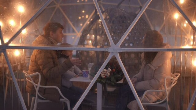 On a pleasantly warm evening, a group of friends comes together in a beautifully lit igloo, savoring wonderful company