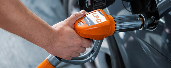 Close-up detail view of fuel autogas pump gun connected with noozle adapter to car tank to refill...