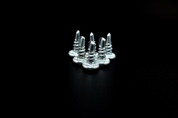 Short metal screws stand in a pyramid on a black background.