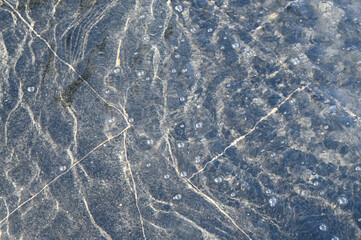 A thin layer of water with ripples on dark marble fountain tiles, illuminated by sunlight. Texture in full screen.