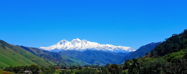 Snow-capped mountains rise above lush valleys under a clear blue sky in a remote landscape