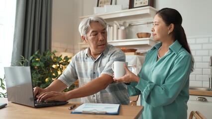 Obraz premium Grandmother holding hot coffee cup and encouraging stressful project manager disappointing about deceasing sales or working problem while old man with casual cloth pointing at laptop screen. Myrmidon.