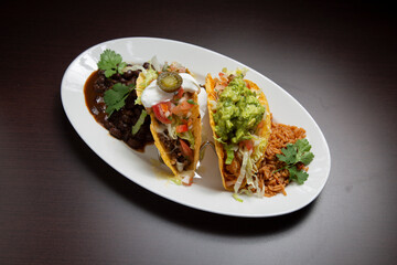 Mexican food platter displaying colorful tacos, garnished with fresh ingredients, served alongside seasoned rice and black beans