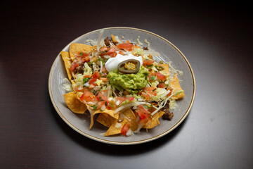Plate of nachos topped with ground beef, guacamole, sour cream, jalapeño, lettuce, tomato, and onion