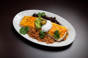 Melted cheese covering loaded burrito, garnished with sour cream, guacamole, jalapenos, accompanied by mexican rice and black beans
