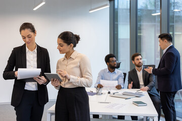 Two businesswomen standing inside the office at their workplace, office workers inside the meeting...
