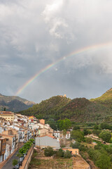 Tiny mountain village under a stormy sky with a vivid rainbow.