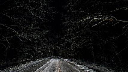 Car lights of night car driving on snowy forest road