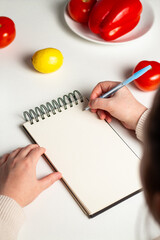 Weight loss diet planning concept. Flat lay of vegetables and notebook. Woman hands writing down meal plan. Mock up.