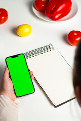 Overhead shot of female creating diet plan for weight loss. Mock up notebook and green screen. Design for healthy lifestyle app, website and nutritionist.