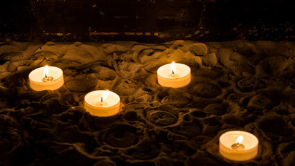 Memorial tealight candles at a church for passed away loved ones. Tealights glowing in the dark background