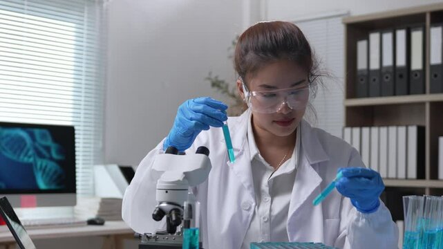 Young female scientist wearing lab coat and protective glasses carefully examining test tubes filled with blue liquid, performing experiments in a modern laboratory setting