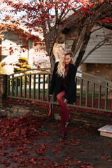 Autumn portrait of a blonde woman in fashionable burgundy clothes walking on the street against the background of a country house outdoors. Selective focus