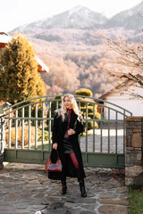 Autumn portrait of a blonde woman in fashionable burgundy clothes walking on the street against the background of a country house outdoors. Selective focus