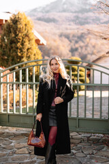 Autumn portrait of a blonde woman in fashionable burgundy clothes walking on the street against the background of a country house outdoors. Selective focus