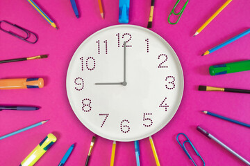 wall clock surrounded by stationery items. 9 o'clock on the dial and pens, pencils, markers in the form of sun rays, as a symbol of the sun, morning, the beginning of the day, Monday