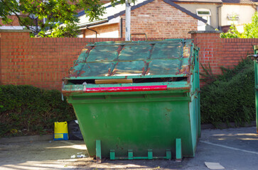 A green dumpster is sitting in front of a brick wall