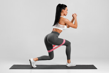 Athletic girl doing exercise for glutes with resistance band on gray background. Fitness woman...