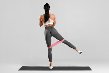 Athletic girl doing exercise for glutes with resistance band on gray background. Fitness woman...