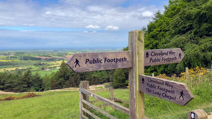 Wooden footpath signs mark the Cleveland Way trail amidst a lush and expansive countryside. The...