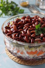 Layered salad Vinaigrette with red beans, pickles, boiled potatoes, beets and carrots in transparent salad bowl on blue background