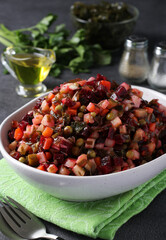 Vinaigrette salad made from beets, potatoes, sea kale, green peas, carrots, pickles, onions and vegetable oil in white bowl on gray background