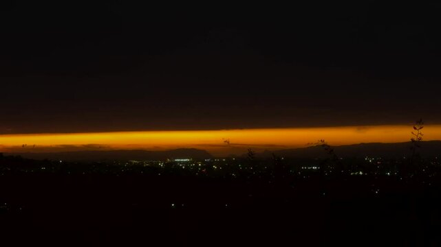 The sun is setting slowly on the horizon of hills and ocean in Auckland, New Zealand.