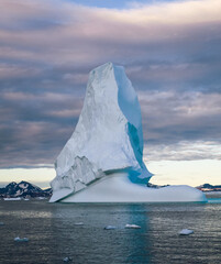 Iceberg in Greenland. Colorful huge Iceberg building. Large ice block floating in the ocean. The sky is cloudy and the sun is setting