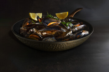Fresh steamed mussels served in a black pan with lemon wedges and parsley garnish. A rustic and elegant seafood dish, perfect for gourmet dining and culinary photography