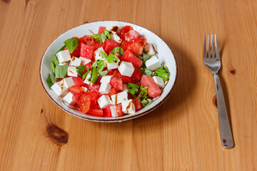 Fresh summer salad with watermelon, tomato, feta cheese and basil on wooden table