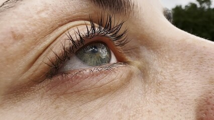 Obraz premium Focus on right green eye of attractive girl blinking and looking up. Portrait of a female pretty face. Calm facial expression of young woman. Tranquil sight of beautiful lady.