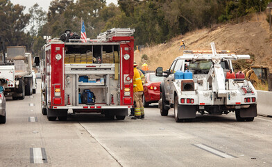 A fire truck stopped on a freeway next to a tow truck at an accident scene. A fireman is visible