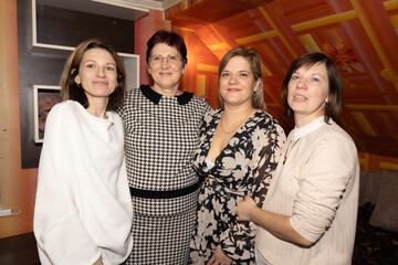 Obraz premium Four women standing together, smiling warmly in an indoor setting. The background features vibrant orange decor. The group exudes positivity and connection.