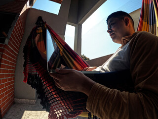 Man lying in a hammock using laptop. Remote work.