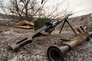 A vintage machine gun and RPG launcher lie on the ground surrounded by barren terrain. A green...