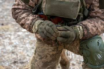Close-up image of two Ukrainian soldiers reloading weapons and unpacking ammunition on the frozen ground. The worn rifle and dusty gear illustrate the harsh realities of front-line service.