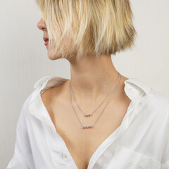 Cropped shot of young blonde woman with straight hair wearing silver chain with a pendant isolated on a gray background. Jewelry with gemstones, holiday accessories