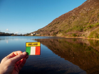 Tourist holding badge with sign Ireland and Irish flag, Kylemore abbey and lake in the background....