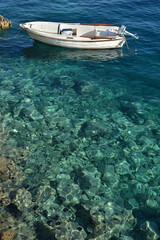 A small white boat floating on crystal clear turquoise sea above a rocky seabed