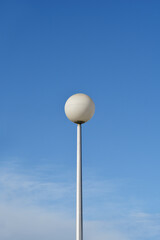 A tall white street lamp with a round globe against a blue sky