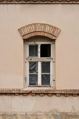 An old, wooden window with an arched brick frame on a dilapidated building facade