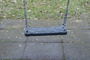 Black swing with decorative relief, hanging on metal chains above a paved playground